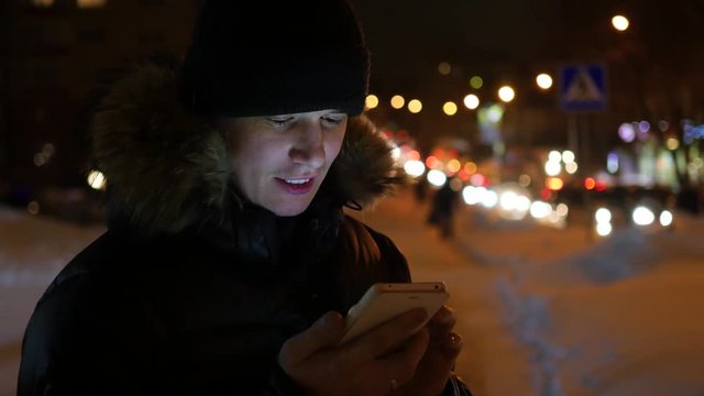Man sms texting using app on smartphone at night in city, winter time.
