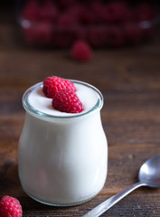White yogurt with raspberries in glass bowl.