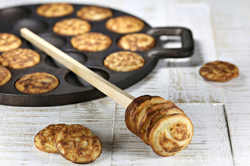 homemade Dutch poffertjes baked in a traditional cast iron pan on wooden background