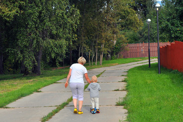 grandmother helps the grandson to go on the scooter, the rear view