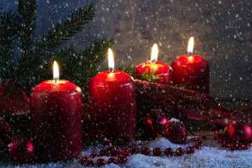 Four red advent candles burning  on a rustic wooden board with snow