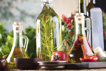 Olive oil and rosemary, chili pepper, many different tomatoes, garlic, red, white, green pepper on old wooden table. Extra virgin olive oil cruets and flavored olive oils with rosemary and chili.