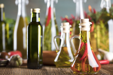 Olive oil and rosemary, chili pepper, many different tomatoes, garlic, red, white, green pepper on old wooden table. Extra virgin olive oil cruets and flavored olive oils with rosemary and chili.