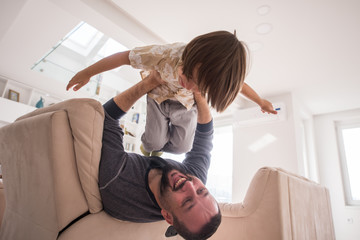 Cheerful young boy having fun with father on sofa