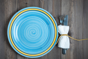 empty blue turquoise round plate with fork and knife wrapped in white napkin on dark wooden...