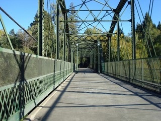 Looking down a walking bridge with green steel railings and overhead stucture. 