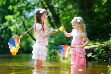 Two cute little sisters playing in a river catching rubber ducks with their scoop-nets