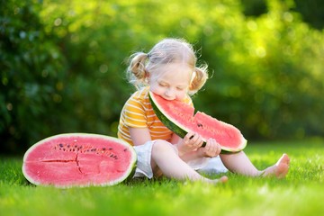 Funny little girl biting a slice of watermelon outdoors