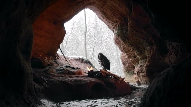 Prehistoric caveman touches snow in times of stone age on background of winter forest