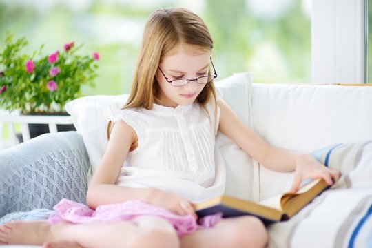 Adorable little girl reading a book in white living room