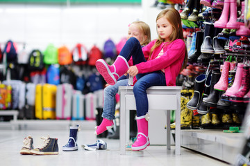 Two little sisters choosing and trying on new rain boots
