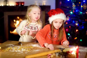 Two adorable little sisters baking Christmas cookies by a fireplace