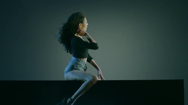 Sexy brunette dances on blue dark background. Beautiful girl dancing, laying on cube.