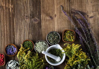 Herbs, berries and flowers with mortar, on wooden table background
