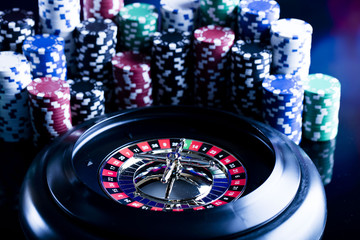 Casino theme. High contrast image of casino roulette, poker game, dice game, poker chips on a gaming table, all on colorful bokeh background. Place for typography and logo.

