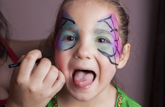 Little girl with tongue out while she is made up by make-up arti