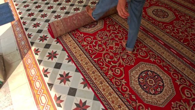 man barefoot rolls out colourful carpet on floor of main muslim mosque in Saigon in Vietnam