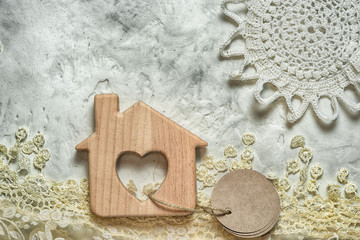 Mortgage concept. Wooden toy house with a window in the shape of a heart, with a knitted lace sun and grass. labels for your inscription.