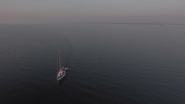 Camera flies over sailboat in magical, still waters on a summer evening.