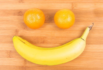Happy fruit face with banana and oranges isolated on wood background