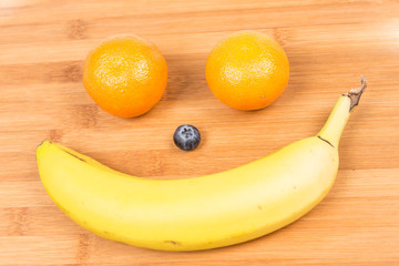 Happy fruit face with banana, blueberry and oranges isolated on wood background