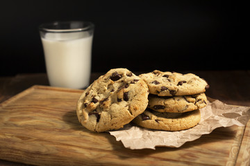 Chocolate cookies on a napkin and a glass of milk, on wooden table. 