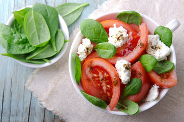 Tomato salad with spinach, cottage cheese, olive oil and pepper on blue wooden background