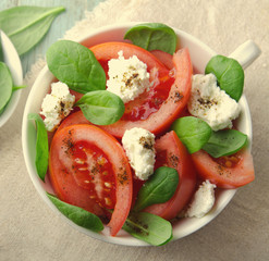 Tomato salad with spinach, cottage cheese, olive oil and pepper on blue wooden background