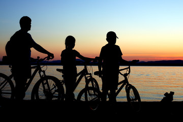 Fototapeta na wymiar Image of sporty family on bicycles outdoors against sunset. Silh