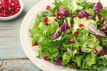 Green salad with spinach, frisee, arugula, radicchio and pomegranate seeds on blue wooden background