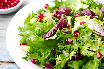 Green salad with spinach, frisee, arugula, radicchio and pomegranate seeds on blue wooden background