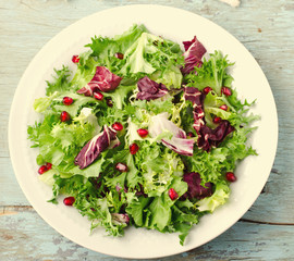 Green salad with spinach, frisee, arugula, radicchio and pomegranate seeds on blue wooden background