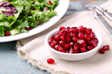 Green salad with spinach, frisee, arugula, radicchio and pomegranate seeds on blue wooden background