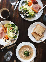 Overhead view of Hotel Breakfast - Soft boiled rice with fried eggs, bacon, sausages, ham, fresh salad, toast and hot tea on top a wooden table 