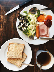Overhead view of Hotel Breakfast - Soft boiled rice with fried eggs, bacon, sausages, ham, fresh salad, toast and hot tea on top a wooden table 