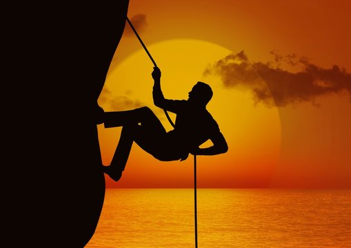Silhouette of man climbing a cliff using rope