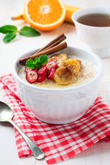 Oat porridge with baked bananas, cinnamon,orange and cranberries in a ceramic bowl for healthy breakfast on a light background. Selective focus.