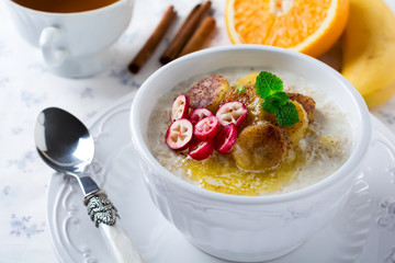 Oat porridge with baked bananas, cinnamon,orange and cranberries in a ceramic bowl for healthy breakfast on a light background. Selective focus.