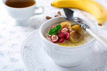 Oat porridge with baked bananas, cinnamon,orange and cranberries in a ceramic bowl for healthy breakfast on a light background. Selective focus.