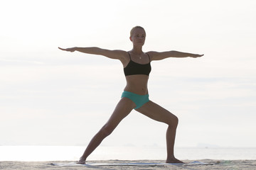 Fototapeta na wymiar Young woman practices yoga on a beach at sunset