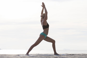 Young woman practices yoga on a beach at sunset