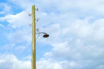 Vintage street lamp on wooden lamppost against blue sky background
