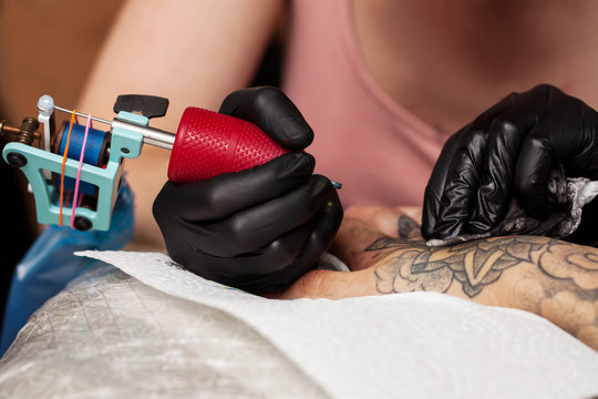 Master tattoo draws the orange paint on the clients tattoo. Tattoo artist holding a pink tattoo machine in black sterile gloves