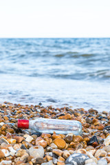 Empty bottle with red cap on stone beach