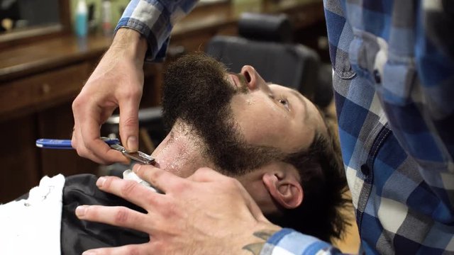 Concentrated Barber shaving beard of client with barber razor