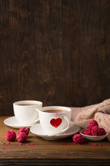 Two cups of hot tea and strawberry chocolate candies on rustic dark wooden background. Valentine's day celebration concept