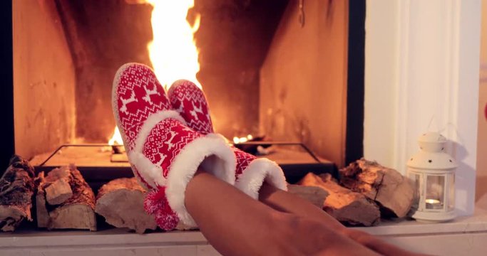 Young woman relaxing in festive red and white Christmas booties with her feet to a blazing fire in a hearth  close up view