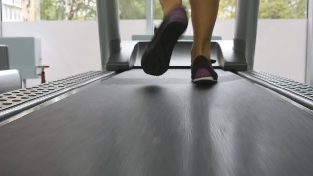 Female legs running on treadmill in gym. Young woman exercising during cardio workout. Feet of girls in sport shoes training indoor at sport club. Close up