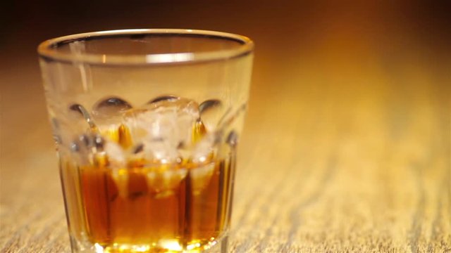 Panning shot of a glass of whiskey with ice cubes, in a pub.