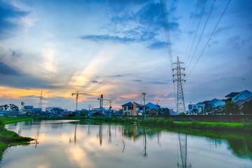 Sunset in urban areas, featuring transmission towers, ponds that make beautiful reflection, crane, rays of light and many houses